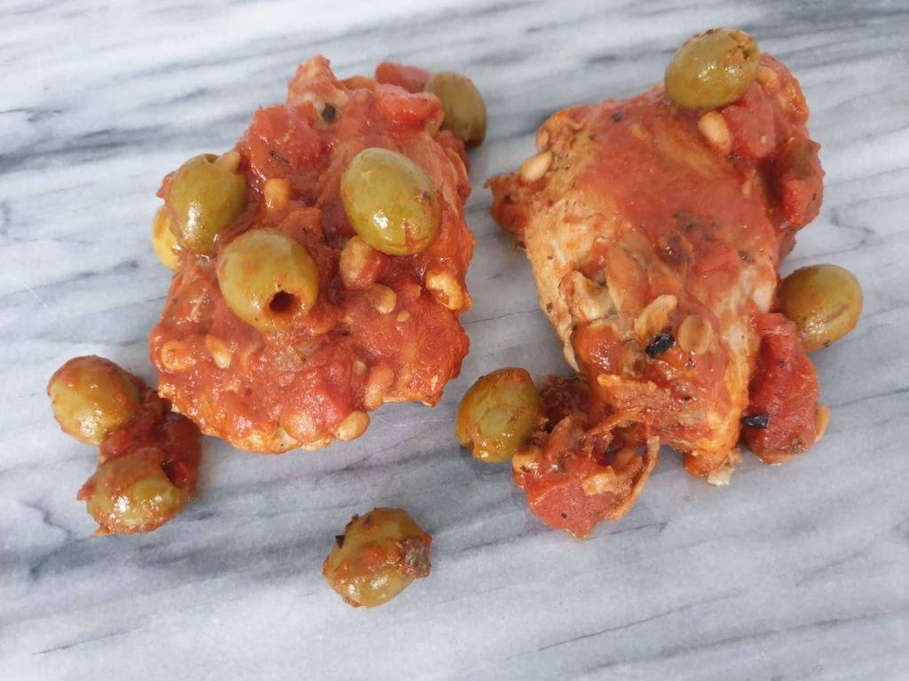 Stukken kip in tomatensaus met olijven op een marmeren ondergrond