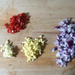 Houten snijplank met stukjes rode ui, chili peper, knoflook en verse gember