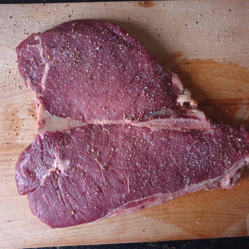 Houten snijplank met steak ingewreven met zout en peper