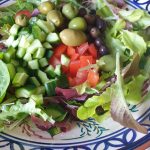 Voeg de tomaten, olijven en komkommer aan de salade toe