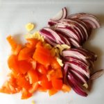Witte snijplank met rode ui, knoflook en tomaat