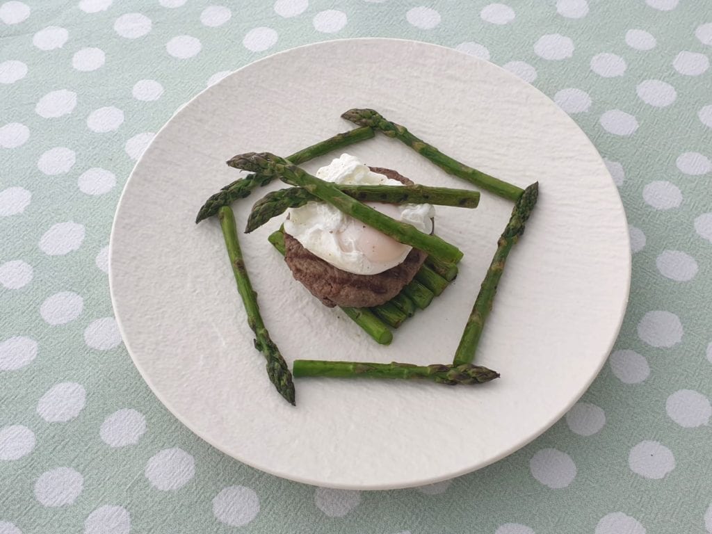 Wit bord met een tartaartje op een bed van groene asperges en een gepocheerd ei