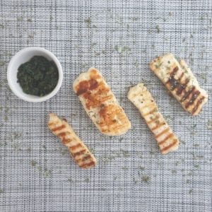 Stukken gegrilde halloumi en bakje met groene kruiden